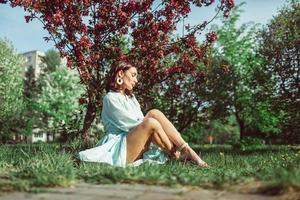 Mädchen sitzt im Park auf dem Gras unter einem blühenden weißen Apfelbaum foto