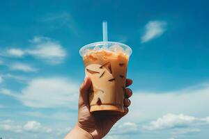 Hand halten vereist Kaffee im ein Plastik Tasse mit ein Blau Himmel und Wolke Hintergrund. ai generiert foto