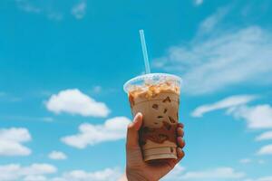 Hand halten vereist Kaffee im ein Plastik Tasse mit ein Blau Himmel und Wolke Hintergrund. ai generiert foto