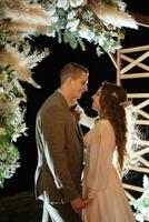 Braut und Bräutigam gegen das Hintergrund von ein Abend Hochzeit Bogen foto