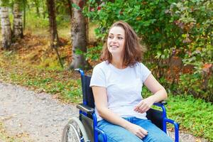 junge glückliche Frau mit Handicap im Rollstuhl auf der Straße im Krankenhauspark, die auf Patientendienste wartet. gelähmtes Mädchen im Rollstuhl für Behinderte im Freien in der Natur. Rehabilitationskonzept. foto