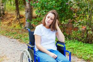 junge glückliche Frau mit Handicap im Rollstuhl auf der Straße im Krankenhauspark, die auf Patientendienste wartet. gelähmtes Mädchen im Rollstuhl für Behinderte im Freien in der Natur. Rehabilitationskonzept. foto