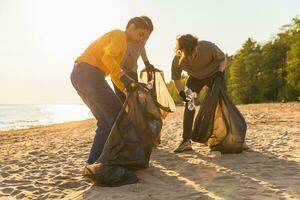 Erde Tag. Freiwillige Aktivisten Mannschaft sammelt Müll Reinigung von Strand Küsten Zone. Gruppe von Menschen setzt Plastik Müll im Müll Taschen auf Ozean Ufer. Umwelt Erhaltung. foto