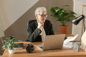 zuversichtlich stilvoll europäisch Mitte alt Senior Frau lesen finanziell Bericht Dokumentation Statistiken. stilvoll älter reifen 60er Jahre grau behaart Dame Geschäftsfrau im Büro. Boss Führer Lehrer. foto