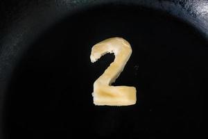 Butter in Form von Nummer 2 auf heißer Pfanne - Nahaufnahme Draufsicht foto