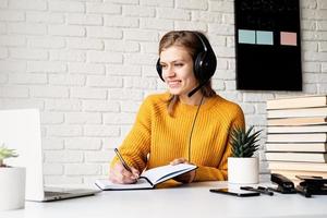 Frau, die online mit Laptop studiert, schreibt im Notizbuch foto