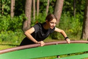 schön jung sportlich Frau im schwarz T-Shirt, schwarz kurze Hose und Rosa Sportschuhe Erwärmen oben ausüben Trizeps und Truhe foto