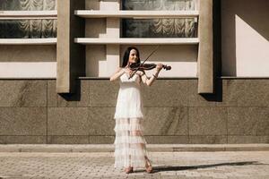 ein Frau Künstler mit dunkel Haar im ein Kleid hält ein hölzern Konzert elektrisch Violine im ihr Hände foto