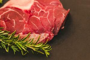 frisch Stück von Fleisch groß Rindfleisch Steak auf das Knochen Markknochen mit ein Zweig von Rosmarin auf ein schwarz Hintergrund foto