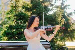 Frau Künstler mit dunkel Haar im ein Kleid Theaterstücke ein hölzern Konzert elektrisch Violine foto