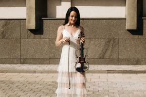 ein Frau Künstler mit dunkel Haar im ein Kleid hält ein hölzern Konzert elektrisch Violine im ihr Hände foto