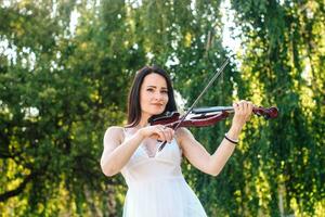 Frau Künstler mit dunkel Haar im ein Kleid Theaterstücke ein hölzern Konzert elektrisch Violine foto