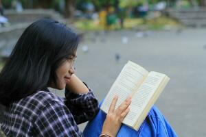 glücklich und Erfolg weiblich asiatisch Hochschule Schüler genießen lesen ein Buch im das Park foto