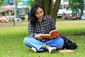 glücklich und Erfolg weiblich asiatisch Hochschule Schüler genießen lesen ein Buch im das Park foto