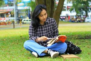 glücklich und Erfolg weiblich asiatisch Hochschule Schüler genießen lesen ein Buch im das Park foto