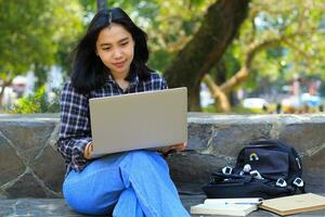 jung lächelnd asiatisch Frau mit Laptop und Schreiben Notizbuch, heiter asiatisch Schüler Aufpassen Webinar und studieren von e Kurs foto