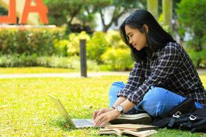 jung lächelnd asiatisch Frau mit Laptop und Schreiben Notizbuch, heiter asiatisch Schüler Aufpassen Webinar und studieren von e Kurs foto