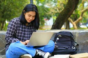 jung lächelnd asiatisch Frau mit Laptop und Schreiben Notizbuch, heiter asiatisch Schüler Aufpassen Webinar und studieren von e Kurs foto