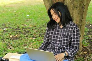 jung lächelnd asiatisch Frau mit Laptop und Schreiben Notizbuch, heiter asiatisch Schüler Aufpassen Webinar und studieren von e Kurs foto