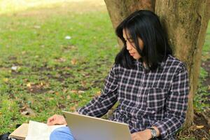 jung lächelnd asiatisch Frau mit Laptop und Schreiben Notizbuch, heiter asiatisch Schüler Aufpassen Webinar und studieren von e Kurs foto