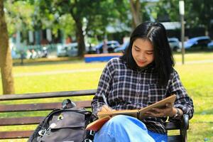 lächelnd asiatisch schön jung Frau genießen Schreiben zu tun aufführen und Idee im Notizbuch im draußen Stadt Park foto