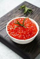 rot Lachs Kaviar im ein Teller auf ein hölzern Schneiden Tafel. grau Beton Hintergrund. Snack Delikatesse. schließen hoch. foto