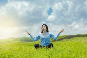 Mädchen Sitzung tun Meditation Yoga im das Feld, Frau tun Yoga draußen, jung Frau tun Yoga auf das Gras im das Feld mit Blau Himmel im das Hintergrund. foto