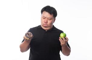 asiatischer Mann, der zwischen Schokoladenkrapfen und grünem Apfel wählt foto