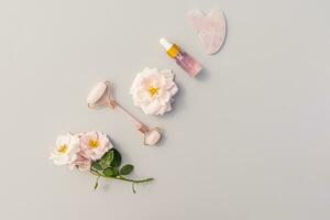 Quarz Rolle, gua sha Schaber, Kosmetik Flasche mit Rose Öl oder Serum zum Gesicht und Hals Haut Pflege und Massage. oben Sicht. eben Layout foto