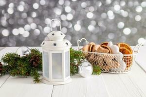 Weihnachten Laterne, Korb mit glasiert Lebkuchen und getrocknet Orange Scheiben, Grün Fichte Geäst auf Weiß hölzern Tisch. ein traditionell behandeln. Bokeh. foto