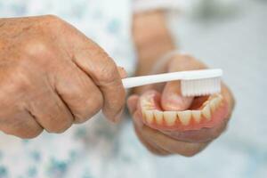 asiatisch Alten Frau geduldig verwenden Zahnbürste zu sauber teilweise Prothese von Ersatz Zähne. foto