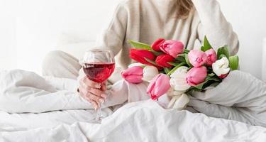 Frau sitzt auf dem Bett im Schlafanzug und hält ein Glas Wein glass foto