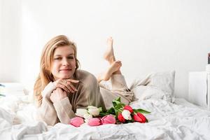glückliche Frau, die auf dem Bett liegt und Tulpenblumenstrauß hält foto