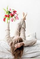 Frau liegt auf dem Bett und hält einen hellen Tulpenblumenstrauß foto