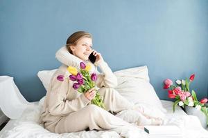 Frau sitzt im Schlafanzug auf dem Bett und telefoniert foto