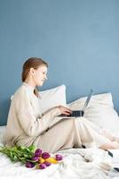 glückliche Frau, die auf dem Bett im Schlafanzug sitzt und auf dem Laptop plaudert foto