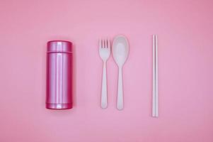 rosa Löffel, Gabel, Stäbchen und Thermosflasche auf rosa Hintergrund foto