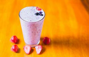 Erdbeere Milchshake auf hölzern Tisch. Erdbeere Smoothie mit Blaubeere auf hölzern Hintergrund. foto