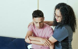 Physiotherapeut Frau auswerten ein Patienten Arm im das Büro, weiblich Physiotherapeut rehabilitieren männlich Patienten Arm. Muskel Rehabilitation Physiotherapie foto