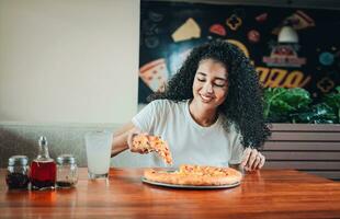glücklich afro Haar Frau Essen Pizza im ein Restaurant. Lebensstil von Afrohaarig Frau genießen ein Pizza im ein Restaurant foto