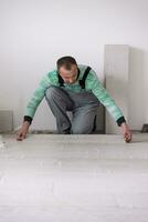 Arbeiter, der die Keramikfliesen in Holzoptik auf dem Boden installiert foto