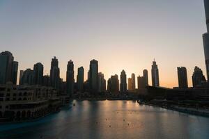 Dubai Singen Brunnen beim Nacht See Aussicht zwischen Wolkenkratzer. Stadt Horizont im Dämmerung modern die Architektur im VAE Hauptstadt Innenstadt. foto