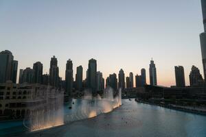 Dubai Singen Brunnen beim Nacht See Aussicht zwischen Wolkenkratzer. Stadt Horizont im Dämmerung modern die Architektur im VAE Hauptstadt Innenstadt. foto