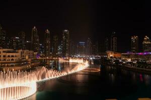 Dubai Singen Brunnen beim Nacht See Aussicht zwischen Wolkenkratzer. Stadt Horizont im Dämmerung modern die Architektur im VAE Hauptstadt Innenstadt. foto