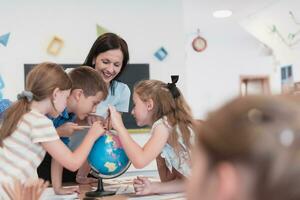 weiblich Lehrer mit Kinder im Erdkunde Klasse suchen beim Globus. Seite Aussicht von Gruppe von vielfältig glücklich Schule Kinder mit Globus im Klassenzimmer beim Schule. foto