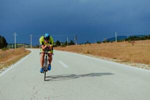 voll Länge Porträt von ein aktiv Triathlet im Sportbekleidung und mit ein schützend Helm Reiten ein Fahrrad. selektiv Fokus foto