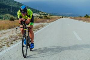 voll Länge Porträt von ein aktiv Triathlet im Sportbekleidung und mit ein schützend Helm Reiten ein Fahrrad. selektiv Fokus foto