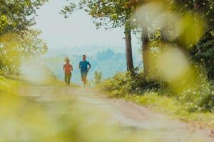 Paar genießen im ein gesund Lebensstil während Joggen auf ein Land Straße durch das schön sonnig Wald, Übung und Fitness Konzept foto