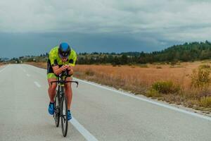 voll Länge Porträt von ein aktiv Triathlet im Sportbekleidung und mit ein schützend Helm Reiten ein Fahrrad. selektiv Fokus foto