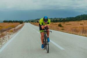 voll Länge Porträt von ein aktiv Triathlet im Sportbekleidung und mit ein schützend Helm Reiten ein Fahrrad. selektiv Fokus foto